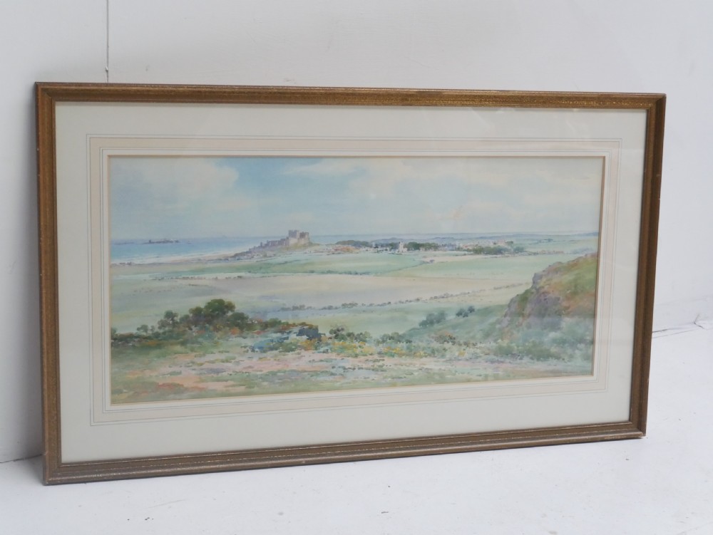 A framed watercolour landscape painting by Frank Wood depicting Bamburgh Castle on the Northumberland coast under a pale sky. View IX
