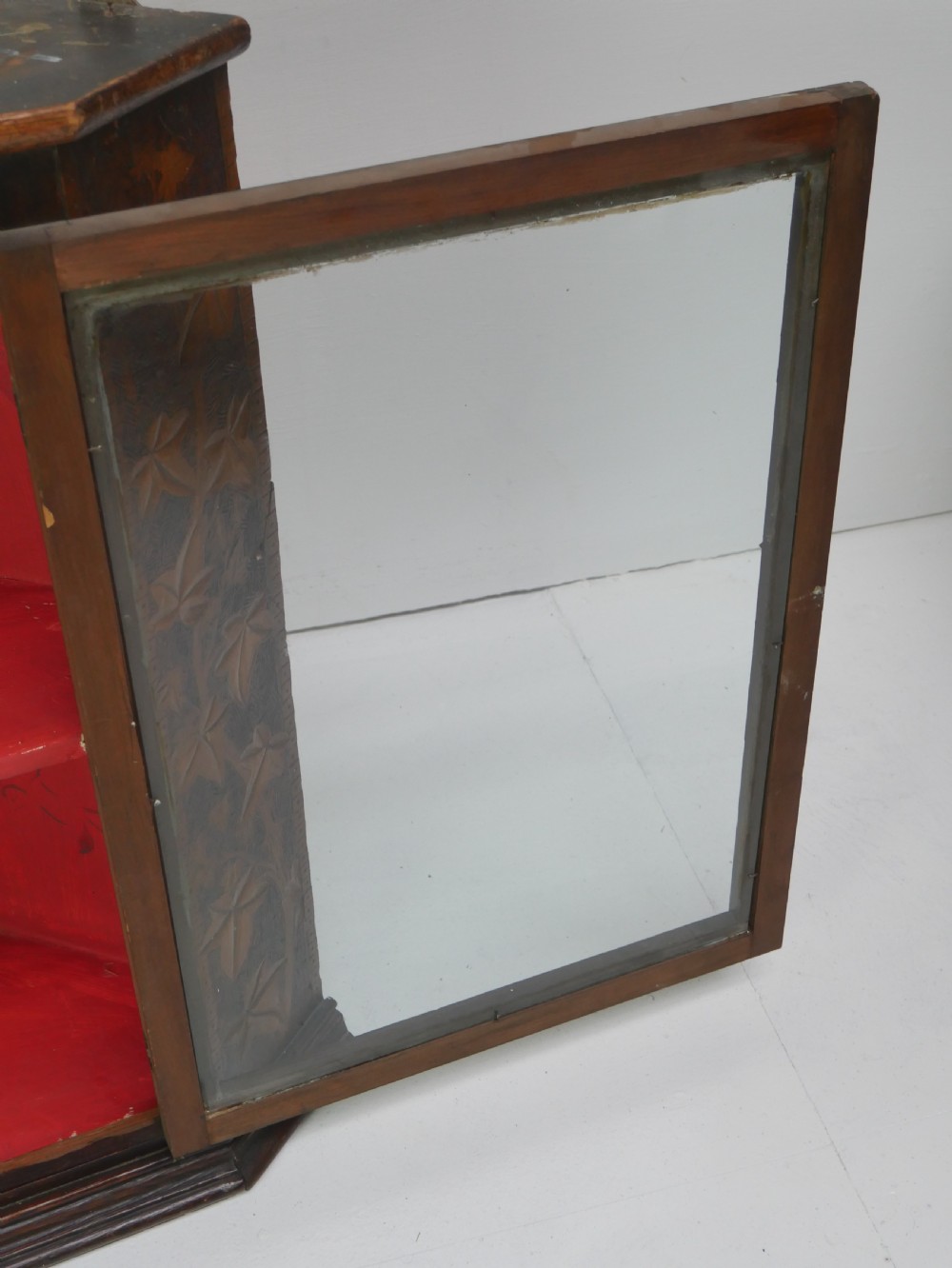 A dark carved wood wall-hanging corner cabinet featuring relief-carved ivy leaves on the side panels, a single glass door, a brass catch, and a red interior. View VI