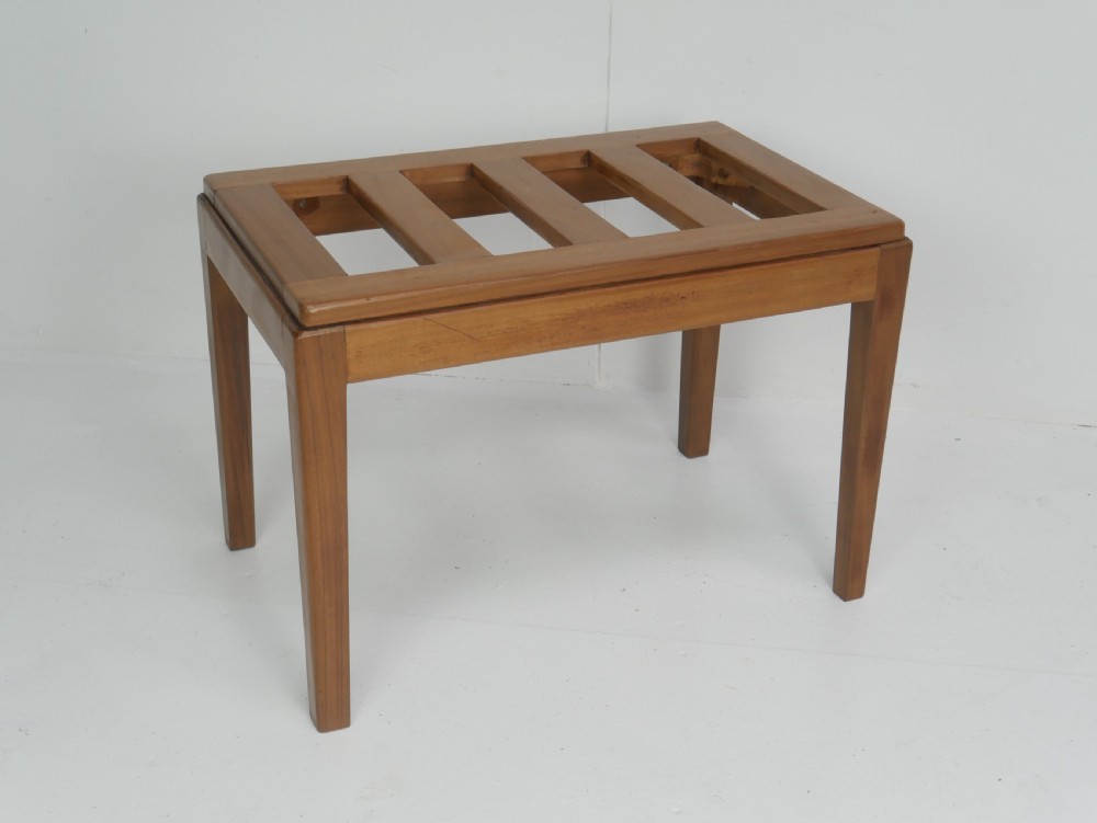 A warm brown wooden luggage rack featuring a slatted rectangular top resting on four square tapered legs.