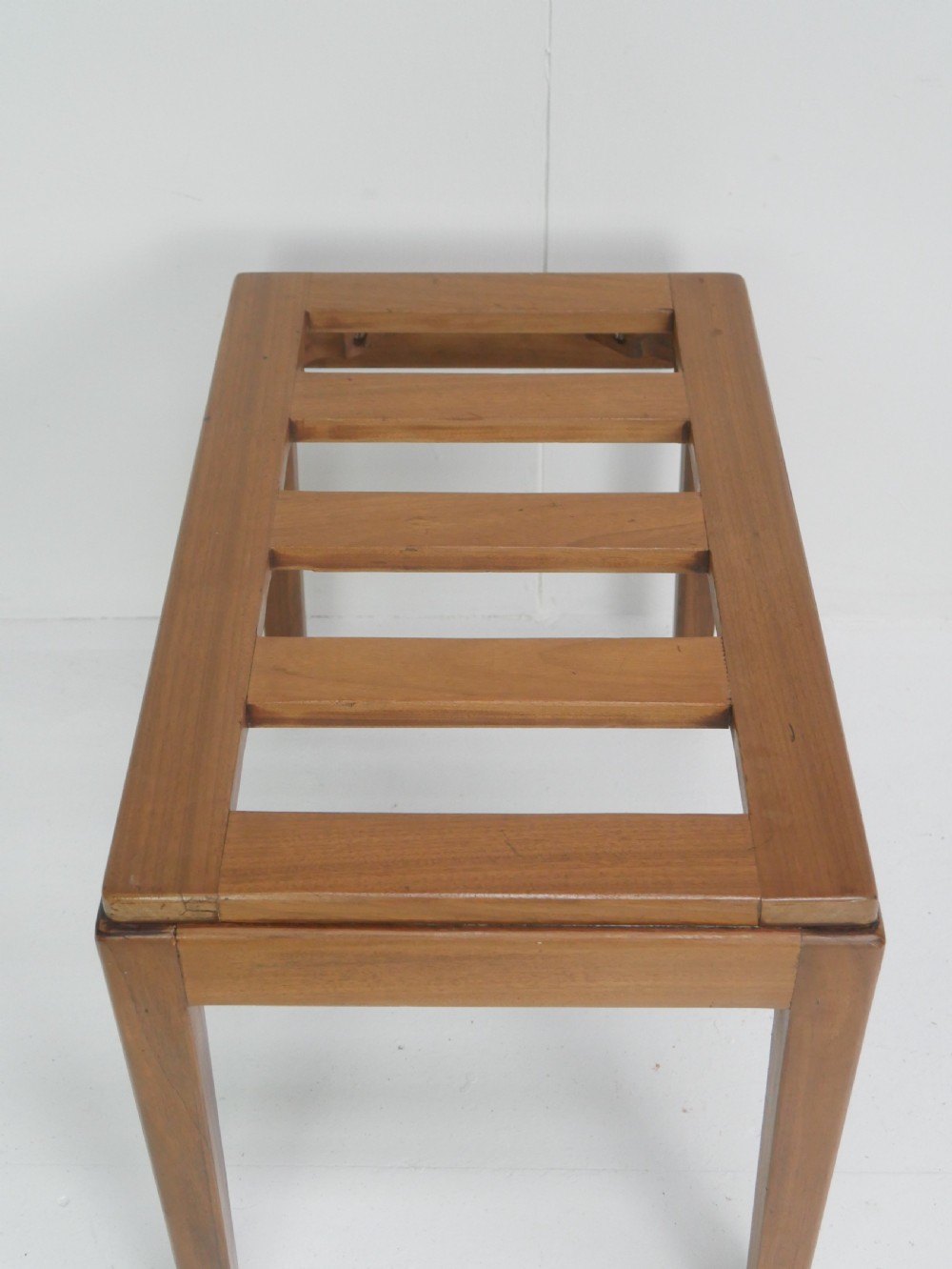 A warm brown wooden luggage rack featuring a slatted rectangular top resting on four square tapered legs. View II