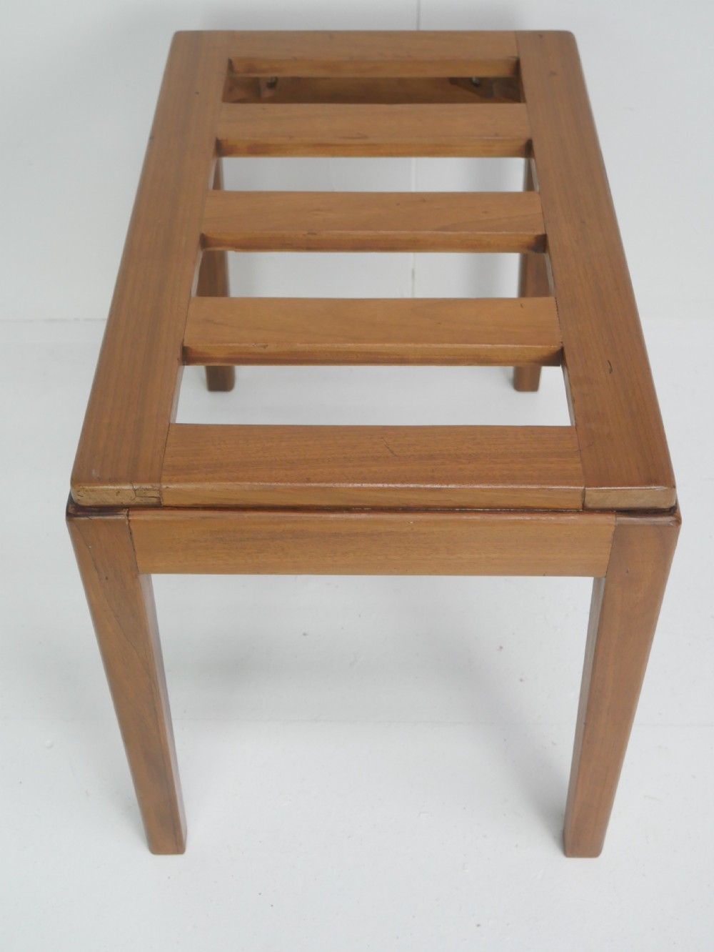 A warm brown wooden luggage rack featuring a slatted rectangular top resting on four square tapered legs. View III