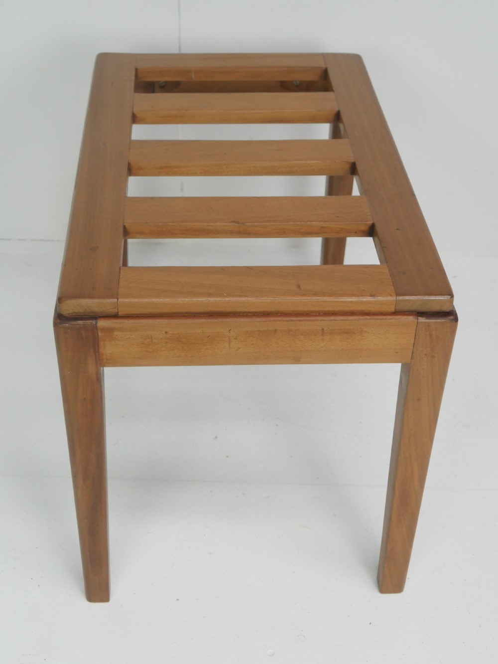 A warm brown wooden luggage rack featuring a slatted rectangular top resting on four square tapered legs. View VI