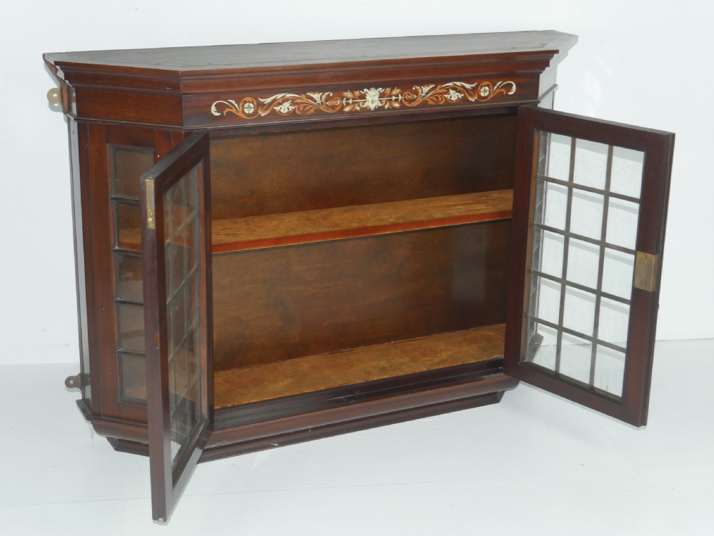 A wall-mounted mahogany display cabinet featuring glazed doors, canted side panels, decorative wood marquetry on the upper frieze, and a brass key escutcheon. View II