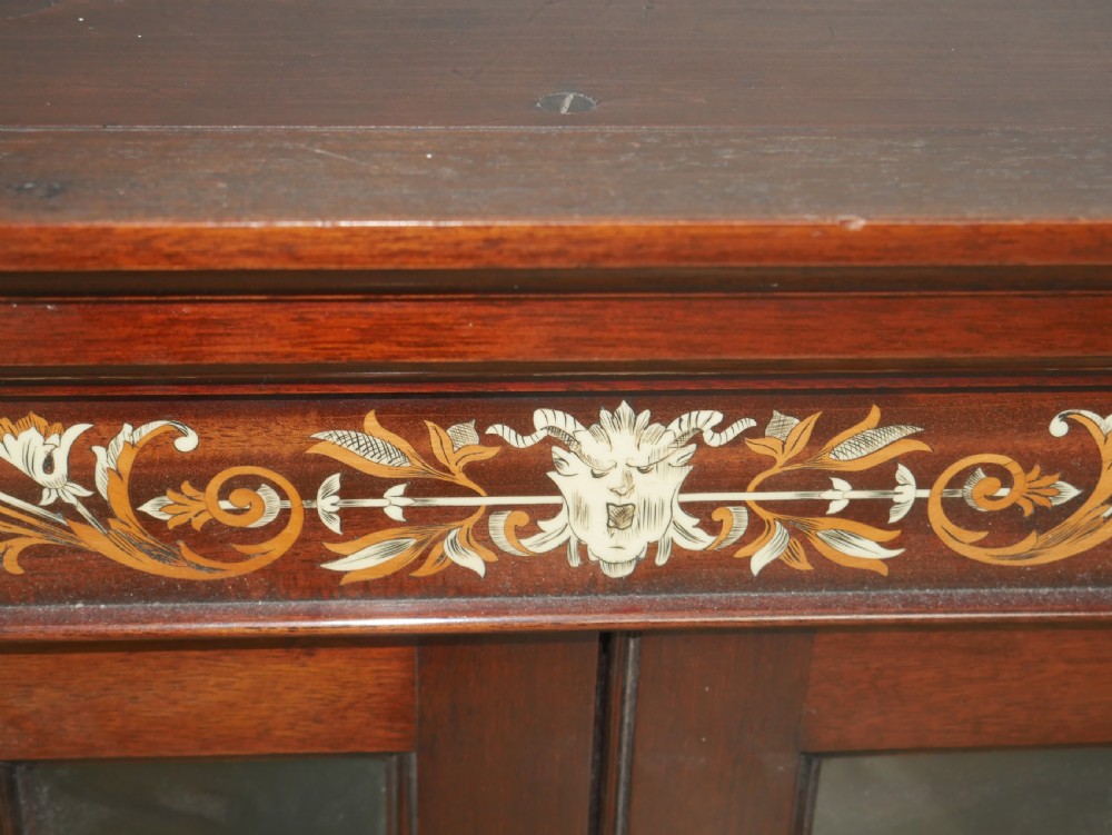 A wall-mounted mahogany display cabinet featuring glazed doors, canted side panels, decorative wood marquetry on the upper frieze, and a brass key escutcheon. View VI