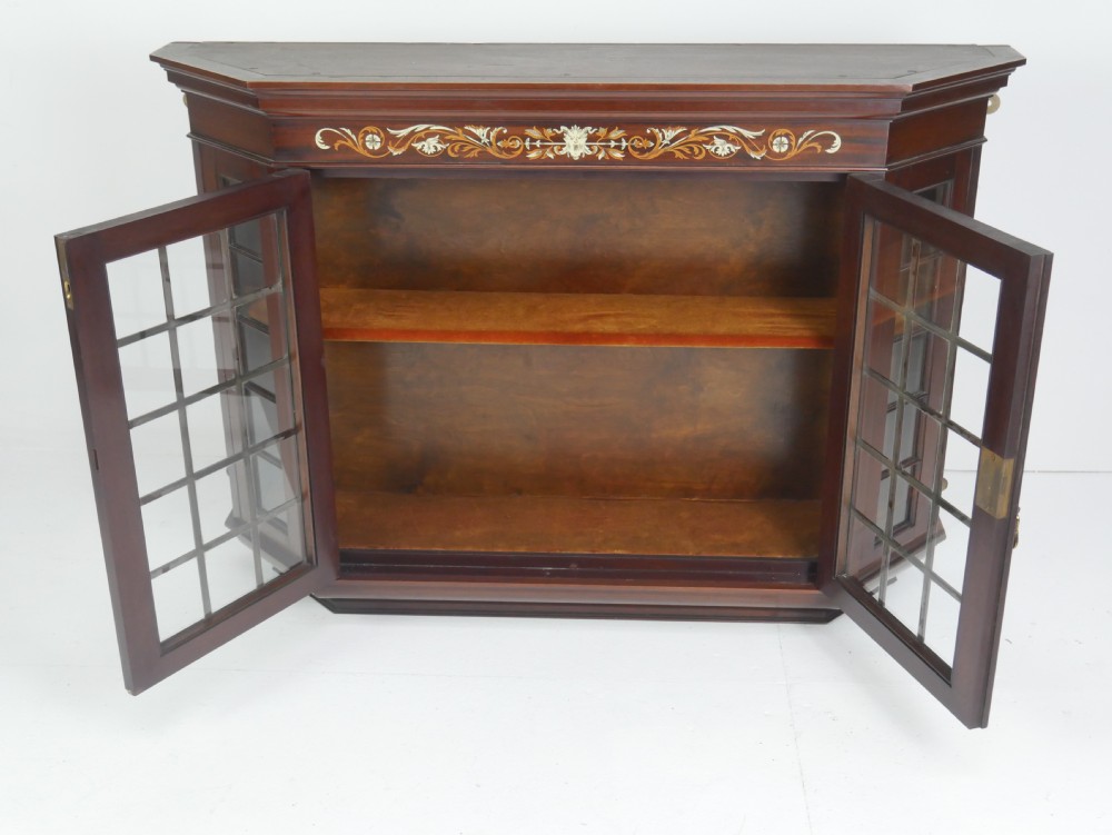 A wall-mounted mahogany display cabinet featuring glazed doors, canted side panels, decorative wood marquetry on the upper frieze, and a brass key escutcheon. View X