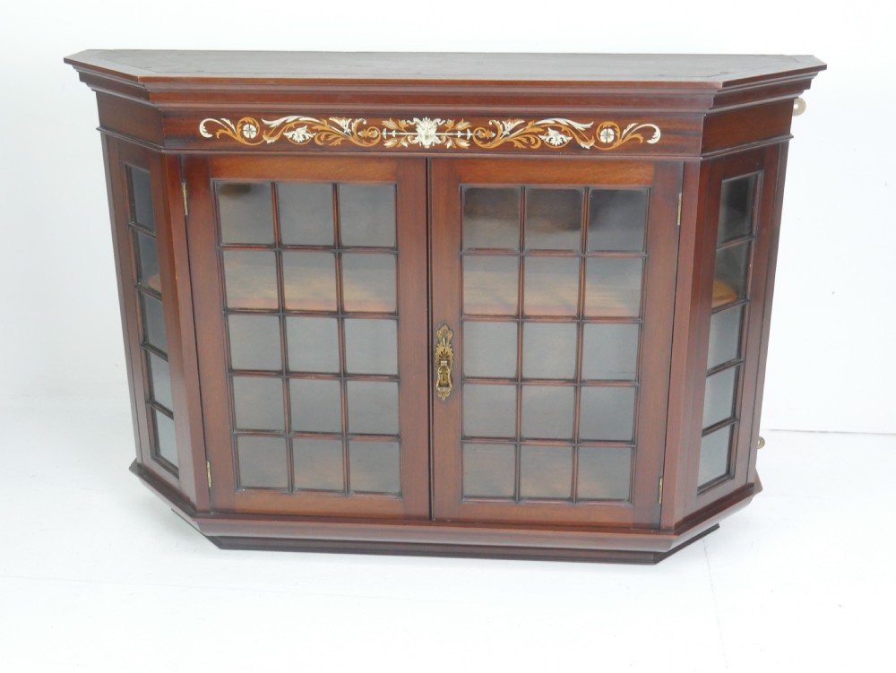 A wall-mounted mahogany display cabinet featuring glazed doors, canted side panels, decorative wood marquetry on the upper frieze, and a brass key escutcheon. View IX