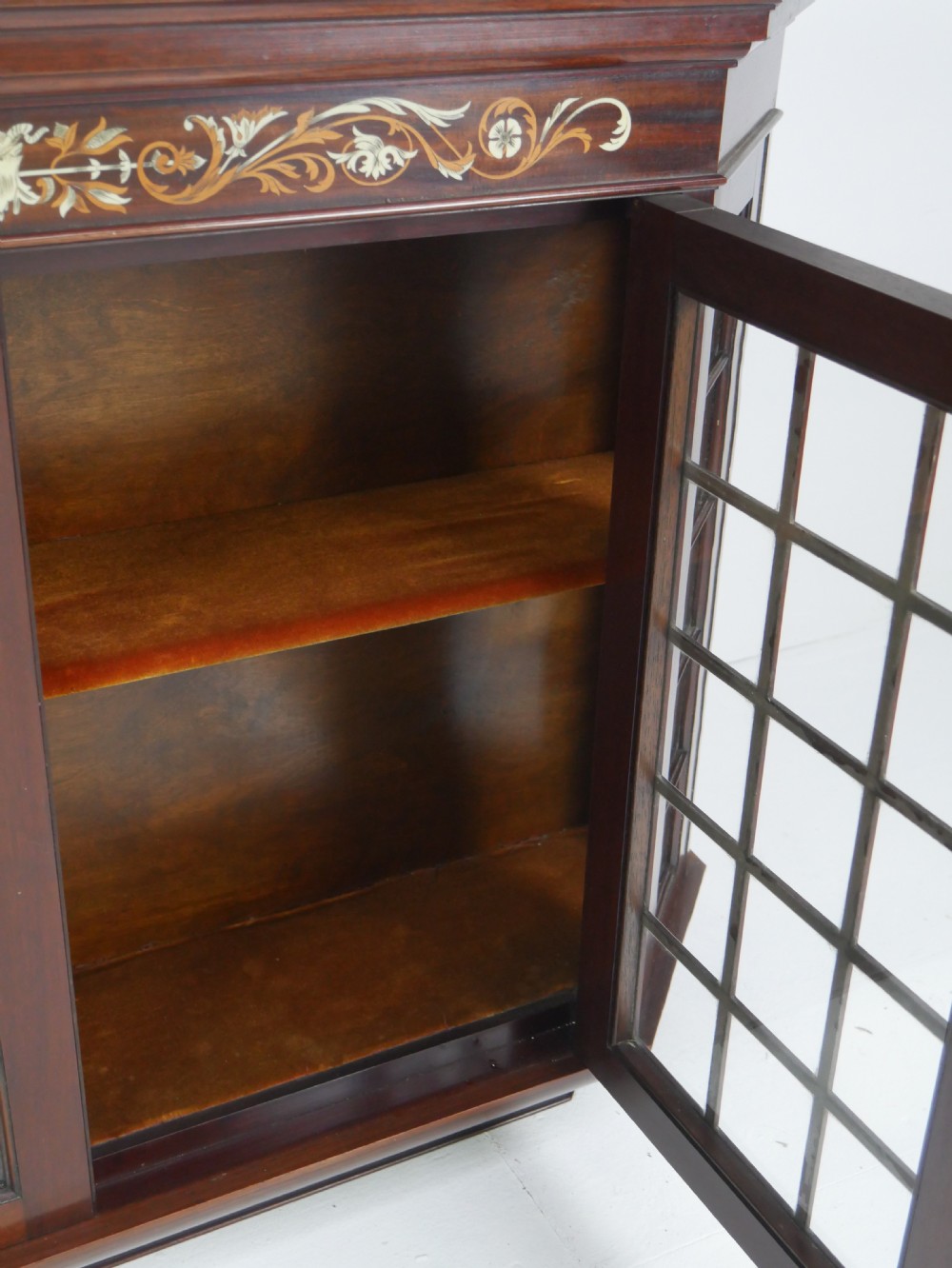 A wall-mounted mahogany display cabinet featuring glazed doors, canted side panels, decorative wood marquetry on the upper frieze, and a brass key escutcheon. View XIV