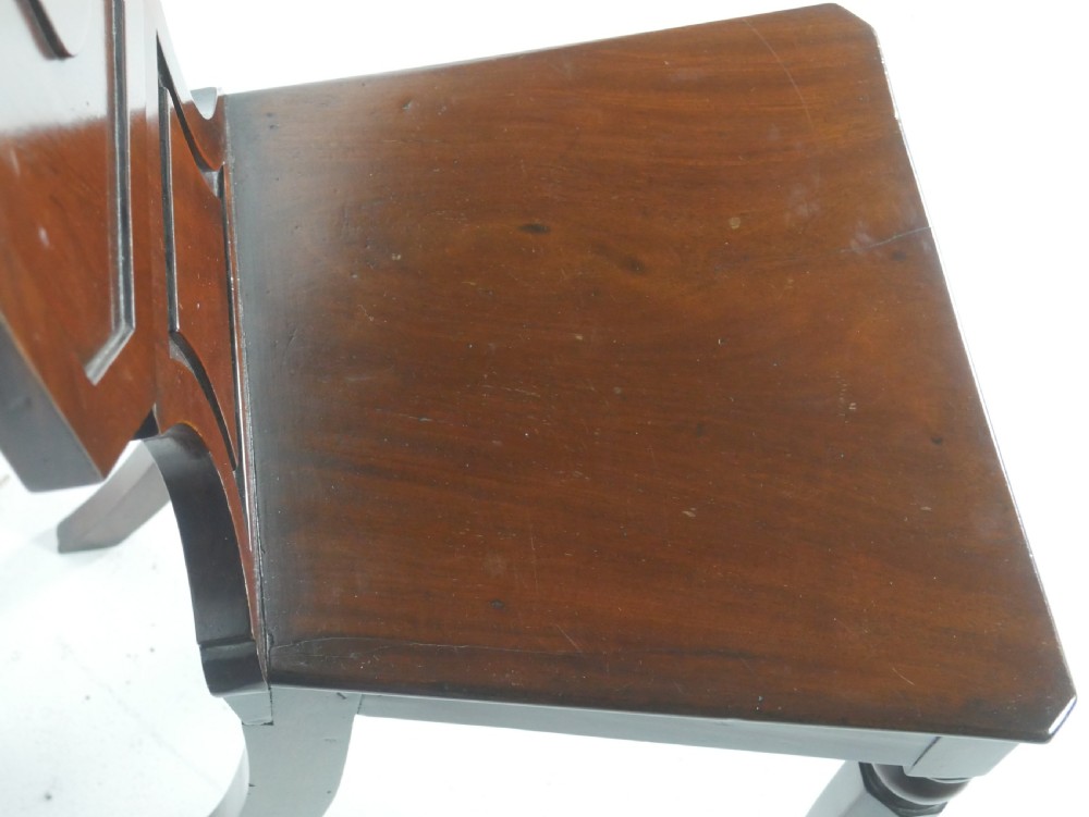 A pair of antique Regency mahogany hall chairs featuring octagonal carved backs with central shield motifs, solid timber seats, and turned front legs. View III