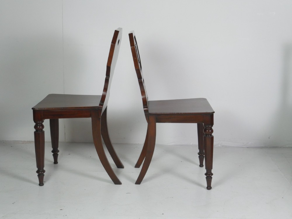 A pair of antique Regency mahogany hall chairs featuring octagonal carved backs with central shield motifs, solid timber seats, and turned front legs. View VII