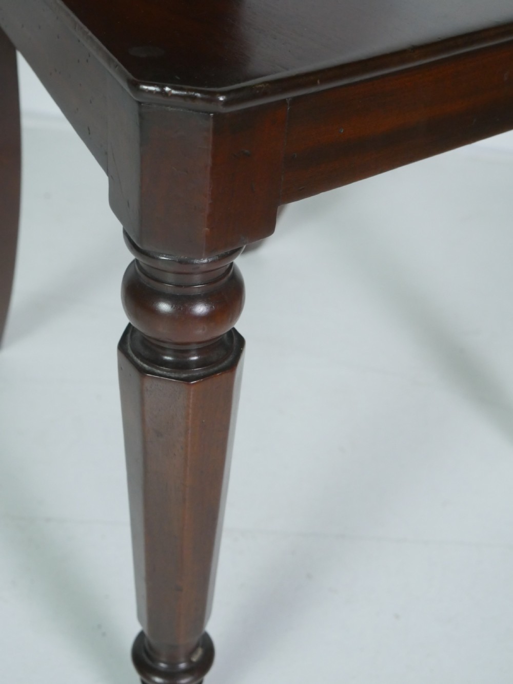 A pair of antique Regency mahogany hall chairs featuring octagonal carved backs with central shield motifs, solid timber seats, and turned front legs. View IX