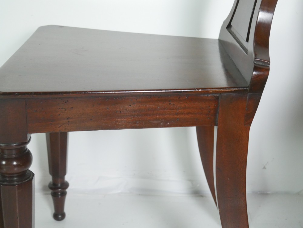 A pair of antique Regency mahogany hall chairs featuring octagonal carved backs with central shield motifs, solid timber seats, and turned front legs. View XIII