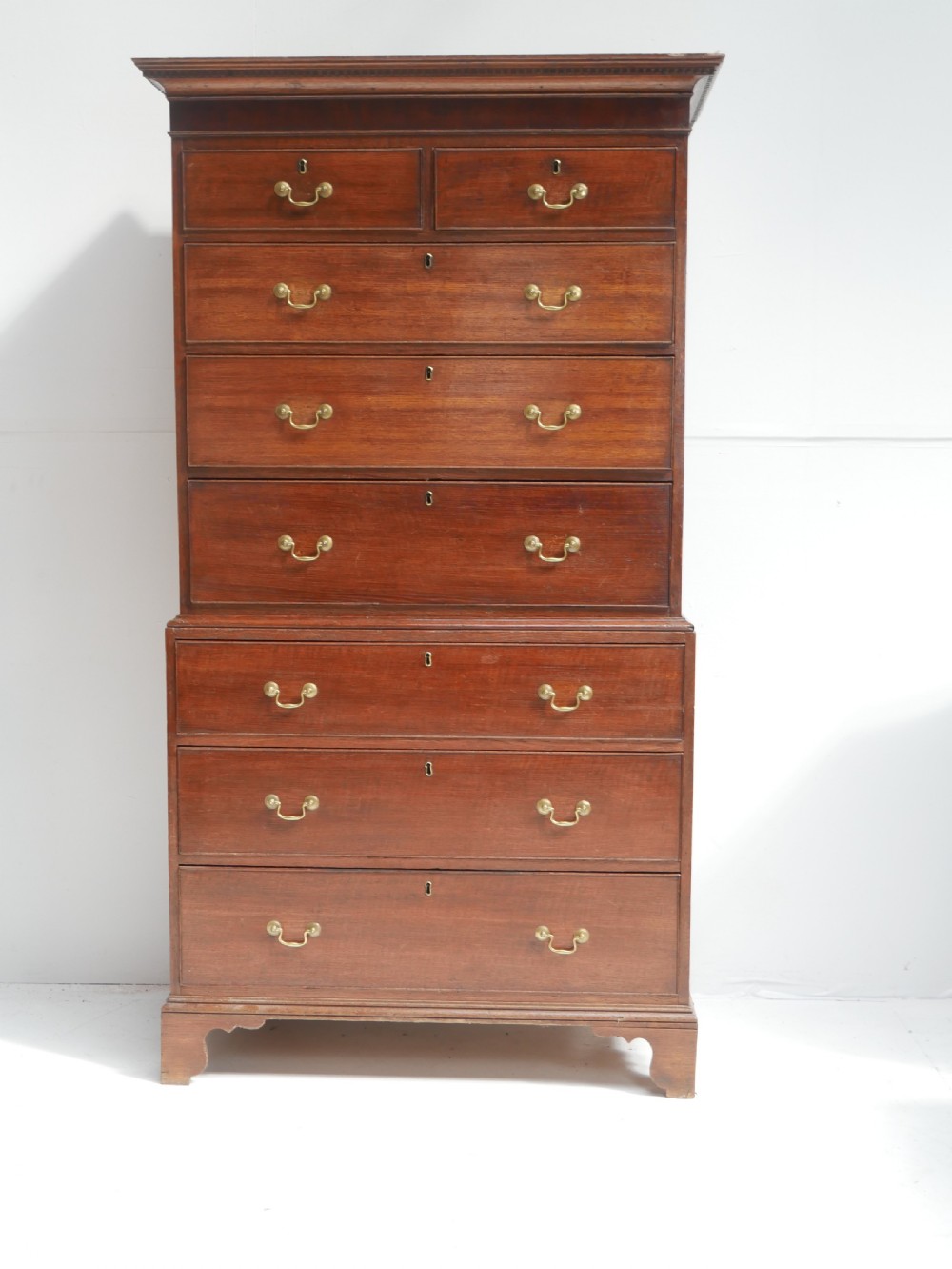 A tall Georgian oak chest on chest featuring brass swan-neck handles, keyhole escutcheons, and bracket feet.