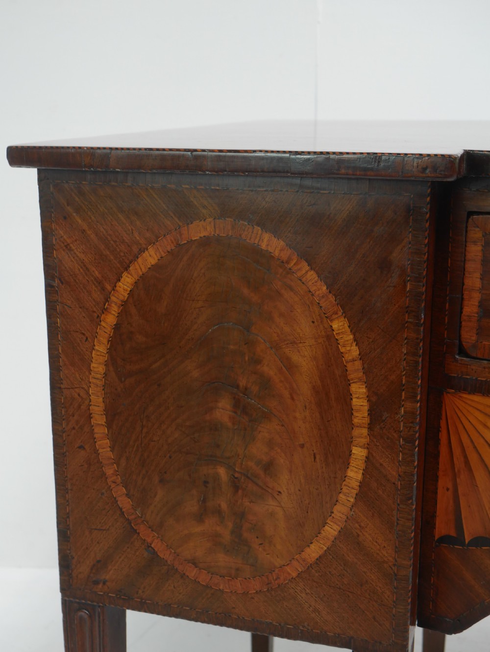 A Georgian mahogany sideboard featuring marquetry fan inlays, oval veneer door panels, a central drawer, and square tapered legs. View III