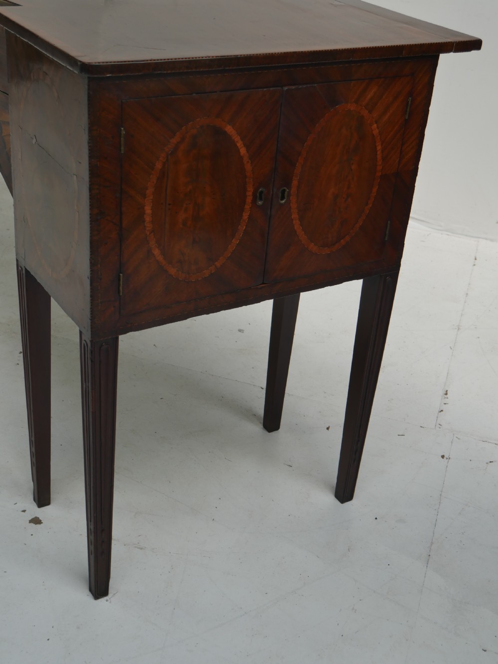 A Georgian mahogany sideboard featuring marquetry fan inlays, oval veneer door panels, a central drawer, and square tapered legs. View VI