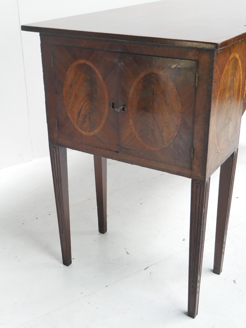 A Georgian mahogany sideboard featuring marquetry fan inlays, oval veneer door panels, a central drawer, and square tapered legs. View IX