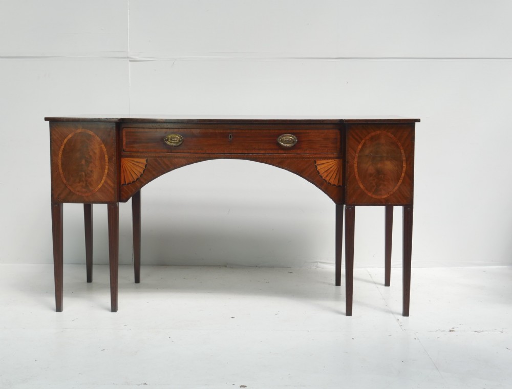 A Georgian mahogany sideboard featuring marquetry fan inlays, oval veneer door panels, a central drawer, and square tapered legs. View XIX