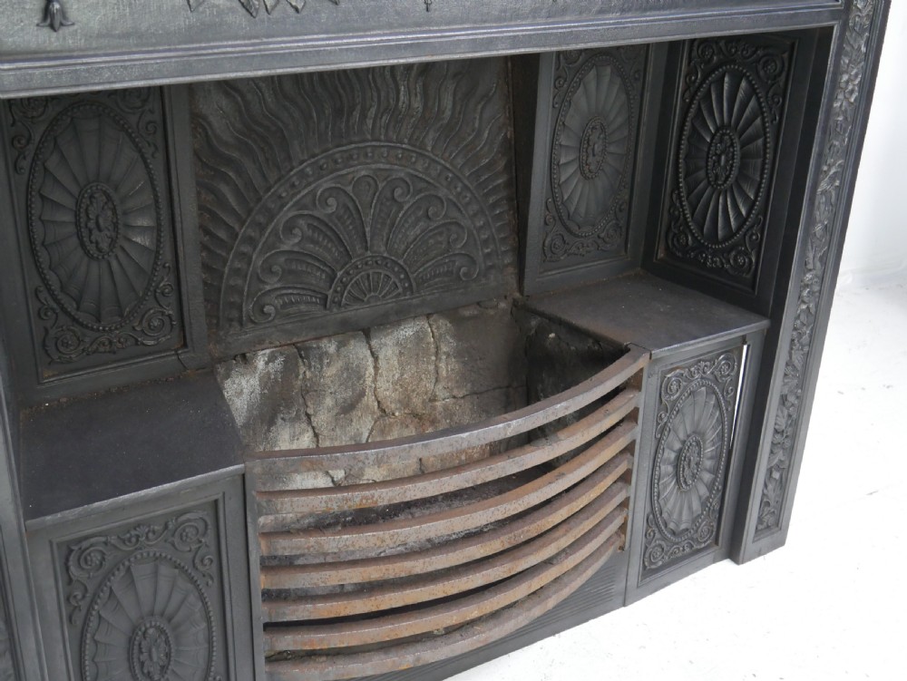 A dark cast iron register grate decorated with carved floral swags, a central profile medallion, and a fan-motif back plate above a curved front grate. View VIII