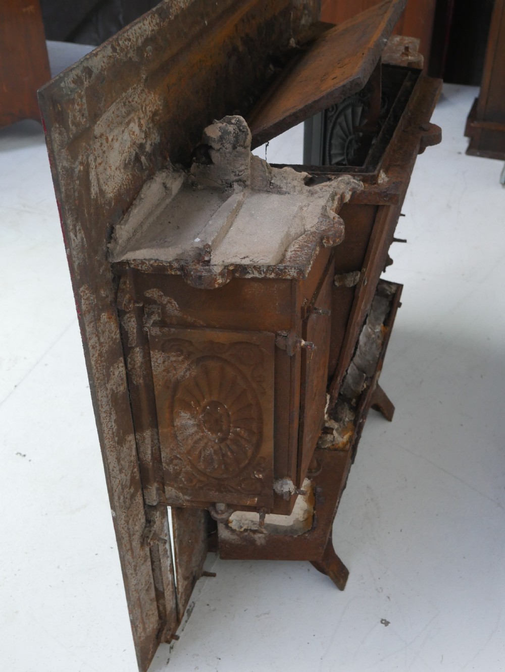 A dark cast iron register grate decorated with carved floral swags, a central profile medallion, and a fan-motif back plate above a curved front grate. View X