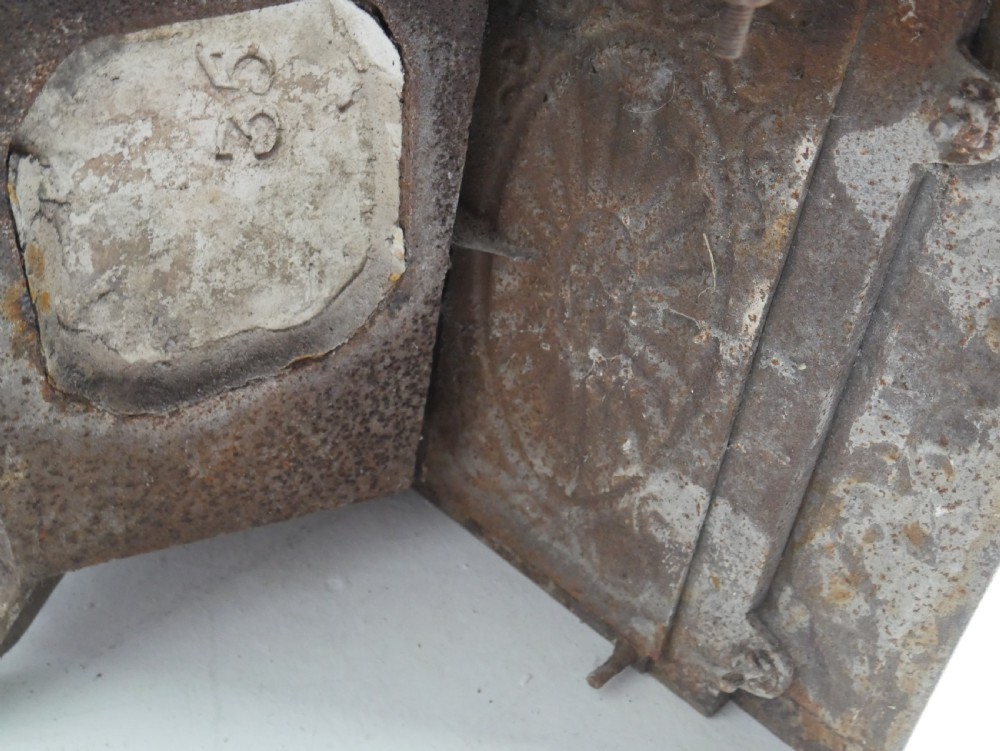 A dark cast iron register grate decorated with carved floral swags, a central profile medallion, and a fan-motif back plate above a curved front grate. View XII
