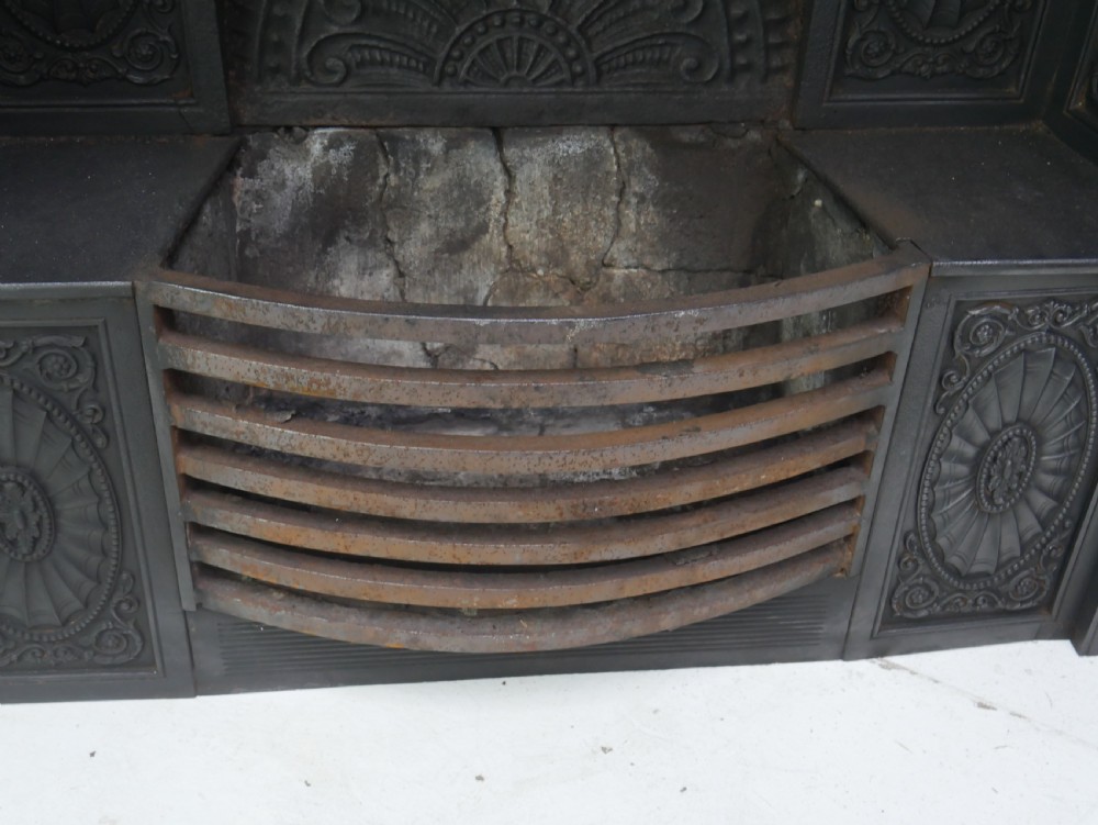 A dark cast iron register grate decorated with carved floral swags, a central profile medallion, and a fan-motif back plate above a curved front grate. View XV