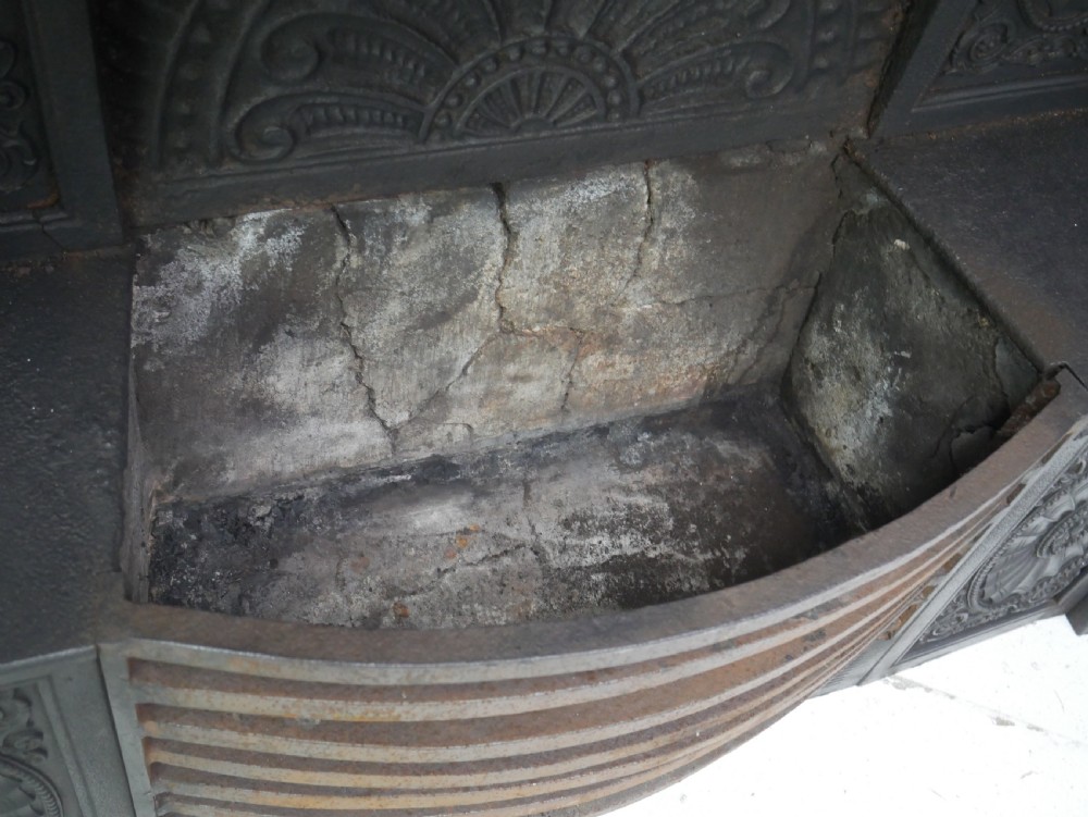 A dark cast iron register grate decorated with carved floral swags, a central profile medallion, and a fan-motif back plate above a curved front grate. View XVI