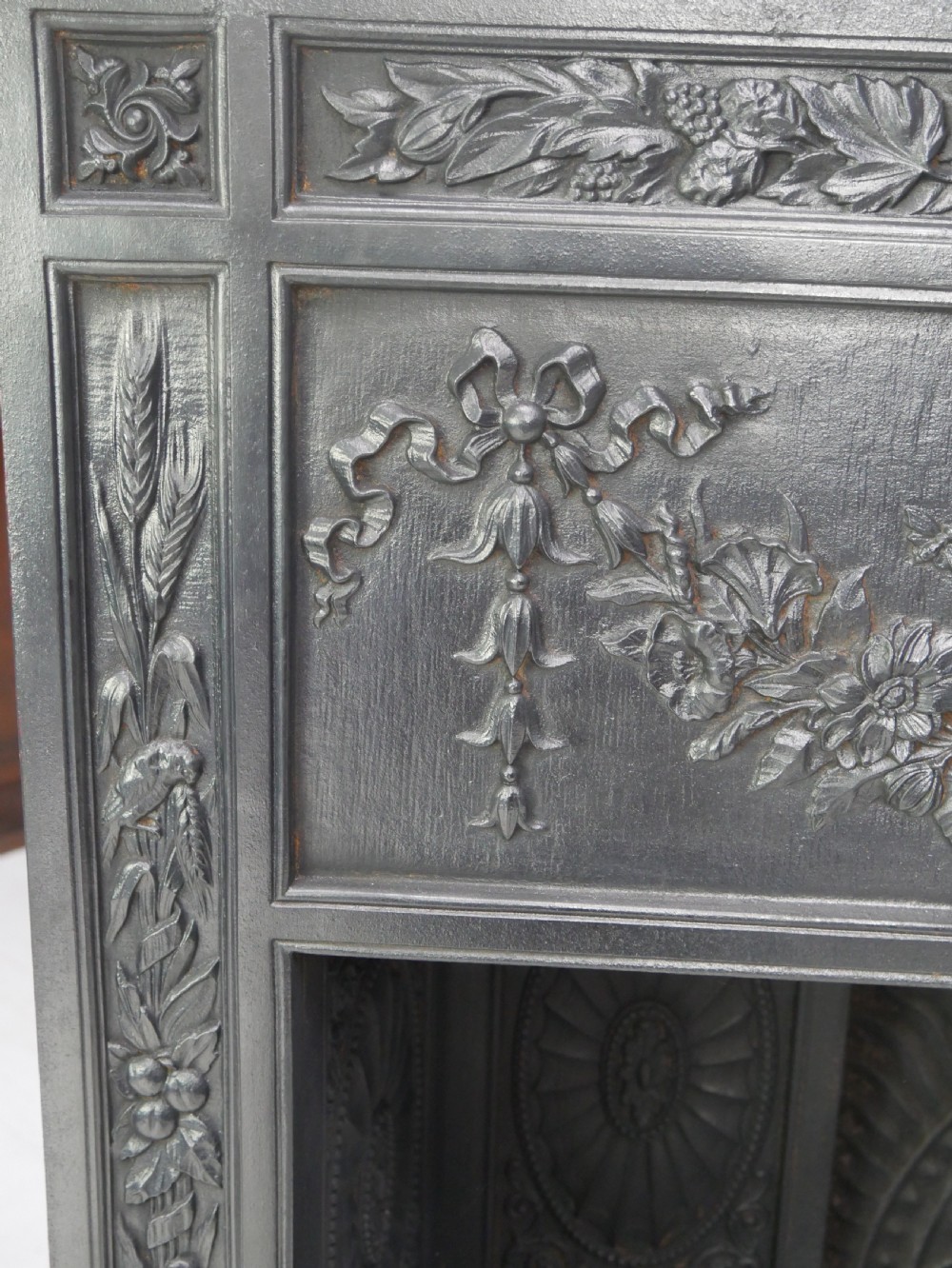 A dark cast iron register grate decorated with carved floral swags, a central profile medallion, and a fan-motif back plate above a curved front grate. View XVII