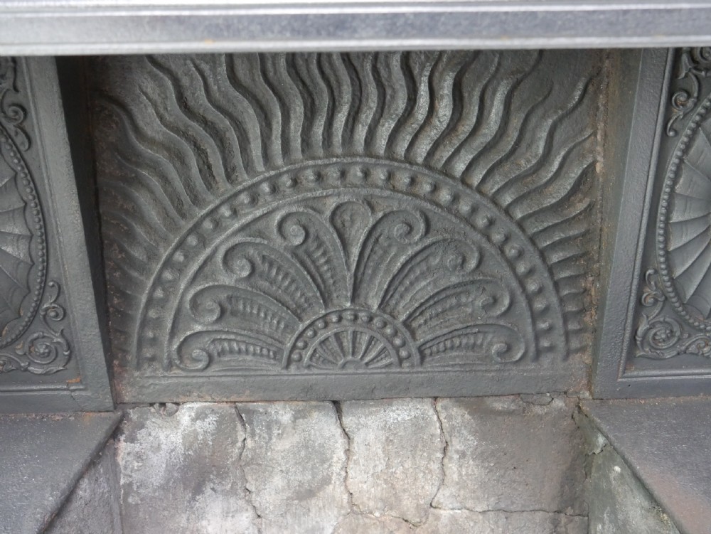 A dark cast iron register grate decorated with carved floral swags, a central profile medallion, and a fan-motif back plate above a curved front grate. View XIX