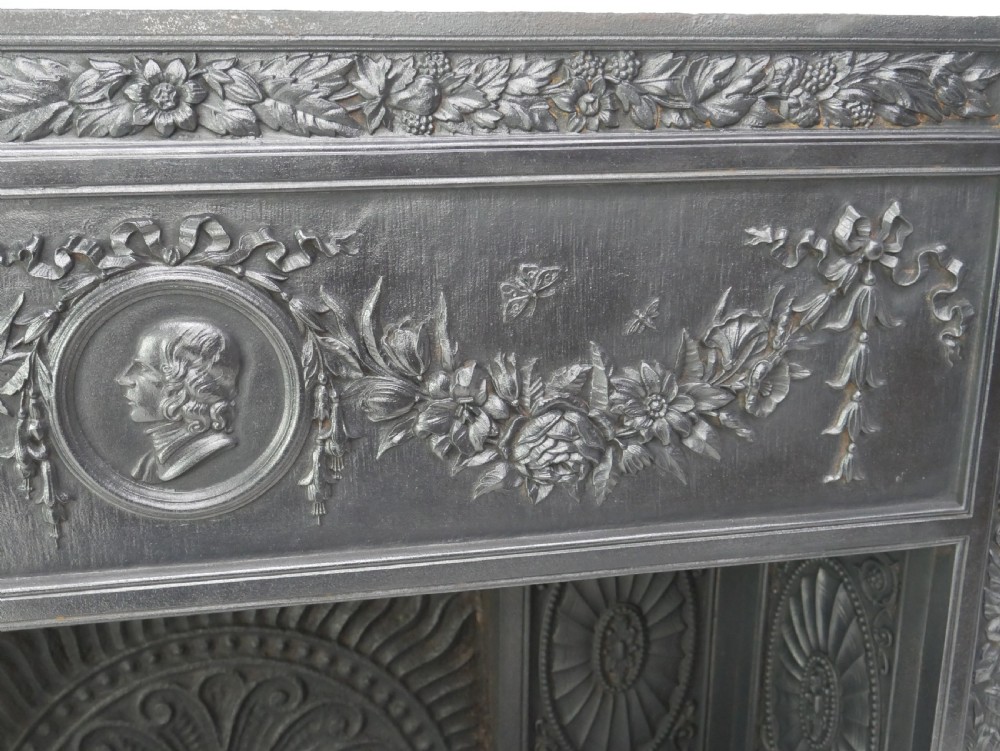 A dark cast iron register grate decorated with carved floral swags, a central profile medallion, and a fan-motif back plate above a curved front grate. View XX