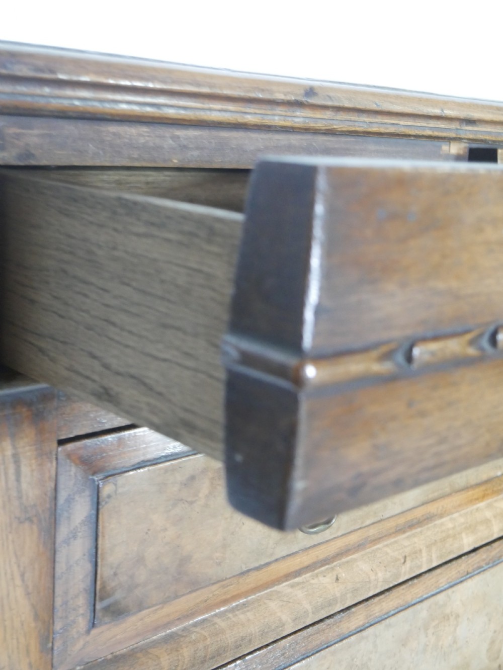 A tall wooden chest of drawers constructed from oak and walnut, featuring five drawers, panelled sides, turned legs with a stretcher base, and brass drop handles. View VII