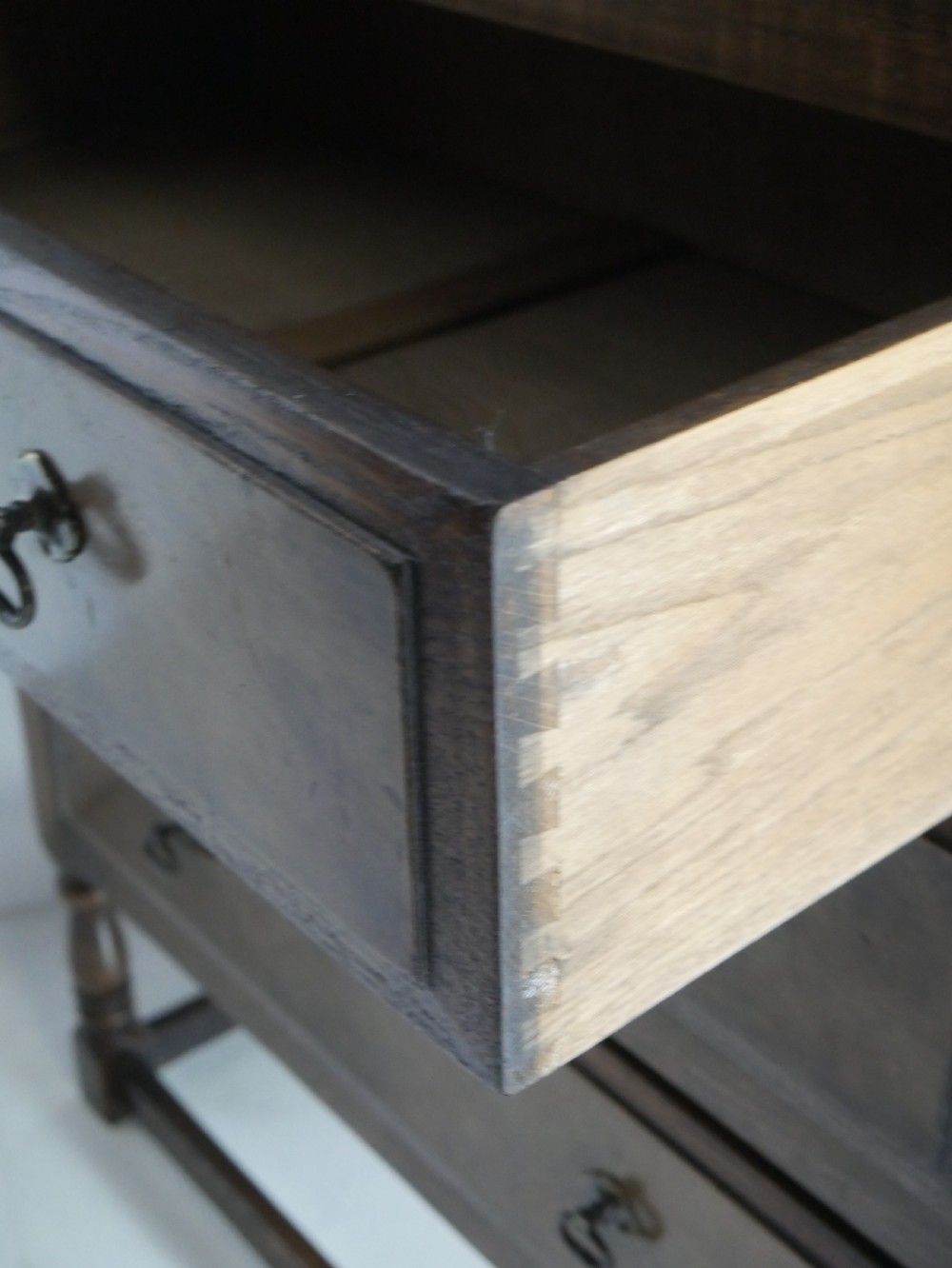 A tall wooden chest of drawers constructed from oak and walnut, featuring five drawers, panelled sides, turned legs with a stretcher base, and brass drop handles. View IX