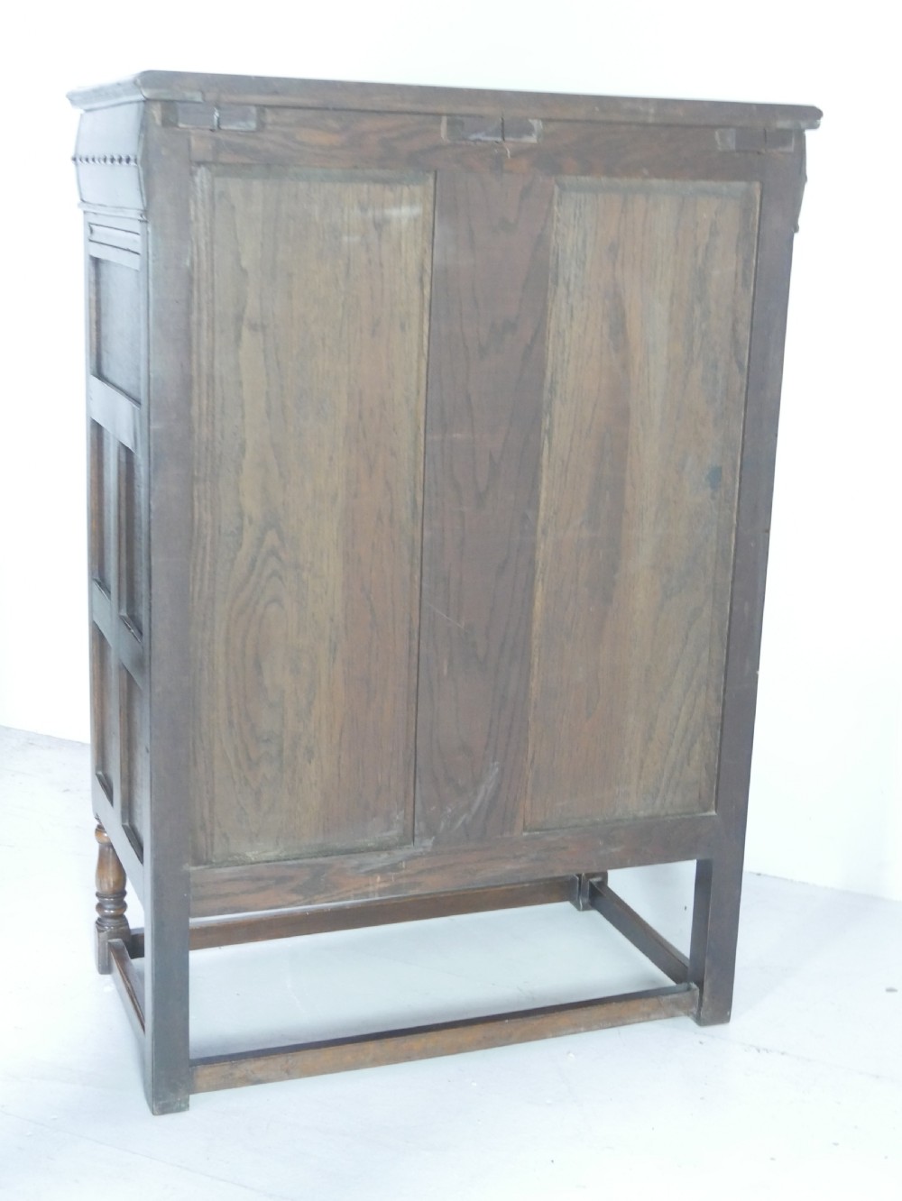 A tall wooden chest of drawers constructed from oak and walnut, featuring five drawers, panelled sides, turned legs with a stretcher base, and brass drop handles. View X