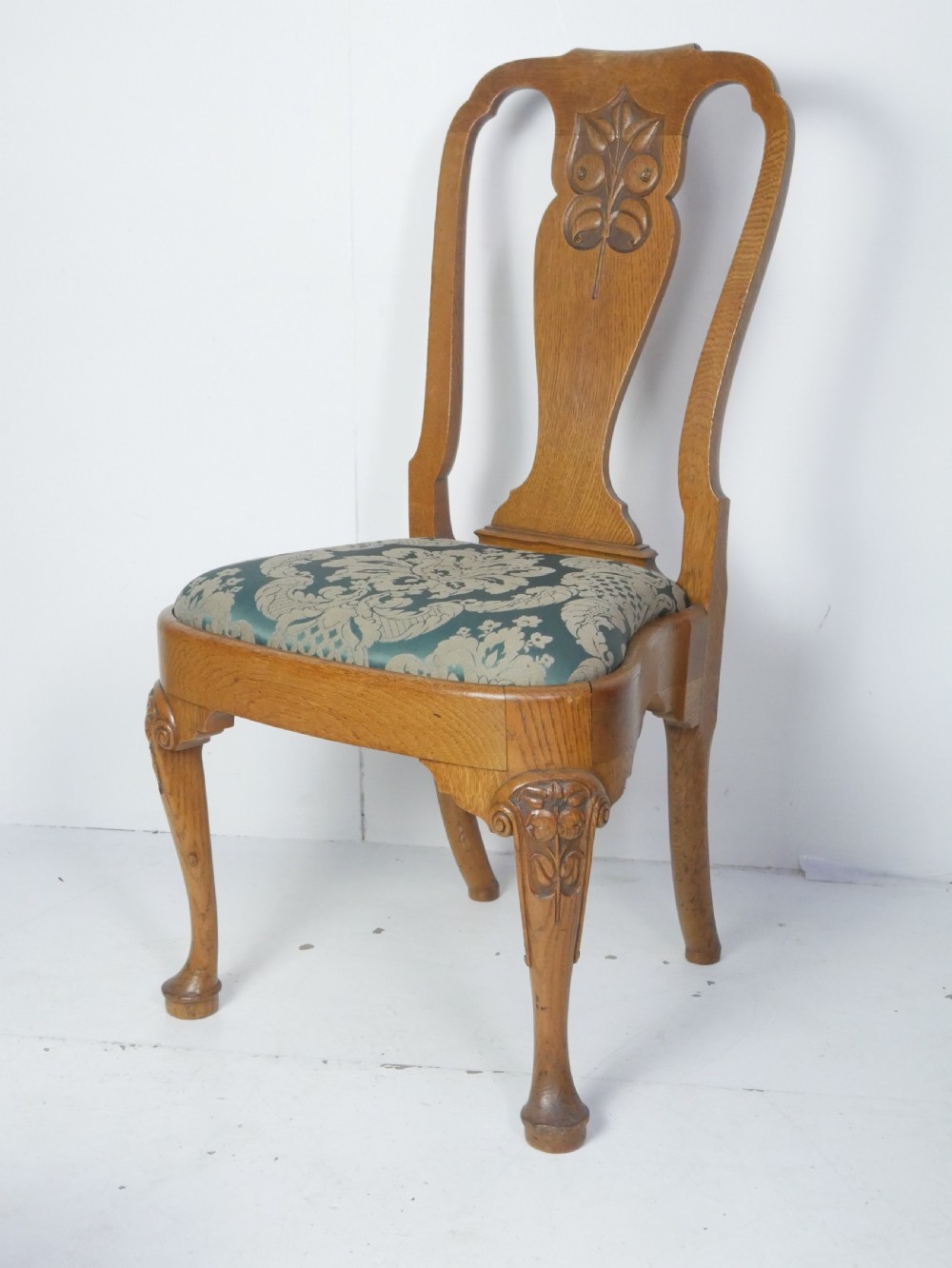 A large set of fourteen carved oak dining chairs featuring shaped back splats, drop-in upholstered seats, and cabriole front legs. View II