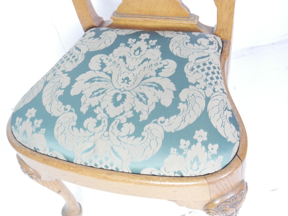 A large set of fourteen carved oak dining chairs featuring shaped back splats, drop-in upholstered seats, and cabriole front legs. View XXI