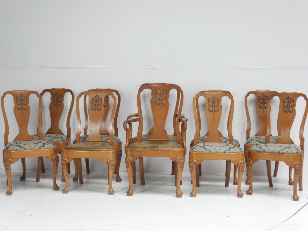 A large set of fourteen carved oak dining chairs featuring shaped back splats, drop-in upholstered seats, and cabriole front legs.