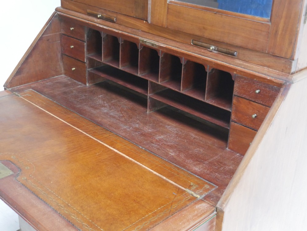 A tall Georgian mahogany bureau bookcase featuring a swan-neck pediment, glazed upper doors, a slant-front writing slope, four long drawers, and bracket feet. View XVI