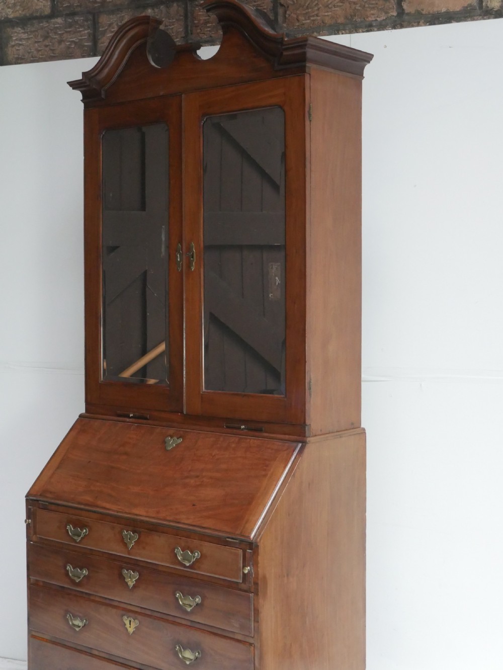 A tall Georgian mahogany bureau bookcase featuring a swan-neck pediment, glazed upper doors, a slant-front writing slope, four long drawers, and bracket feet. View XX
