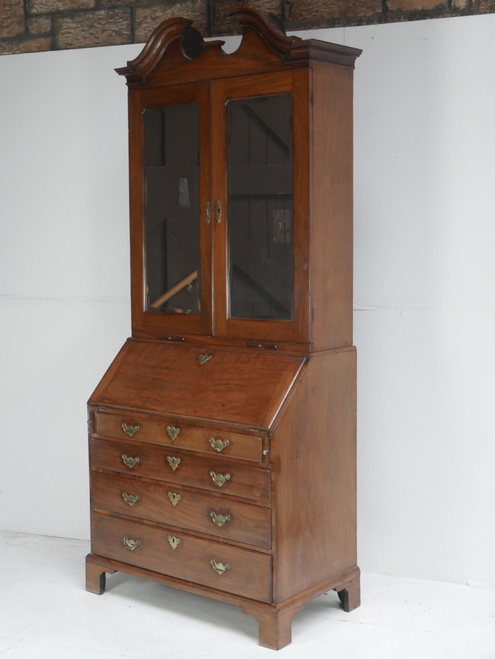 A tall Georgian mahogany bureau bookcase featuring a swan-neck pediment, glazed upper doors, a slant-front writing slope, four long drawers, and bracket feet. View XXI
