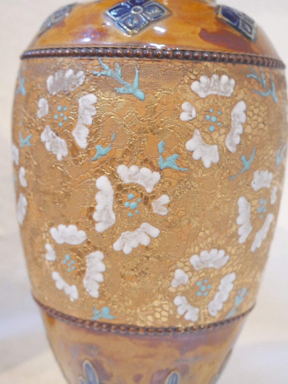 A pair of antique Royal Doulton stoneware vases featuring caramel brown glazing, white floral decorations, and blue foliate accents around the base. View II