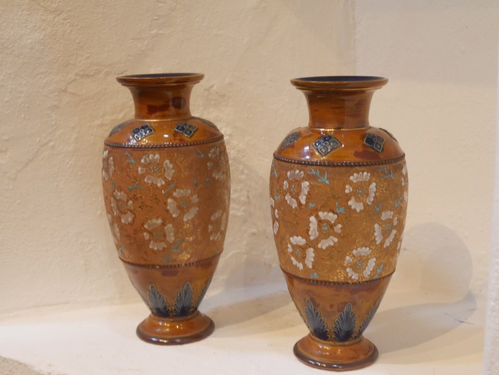 A pair of antique Royal Doulton stoneware vases featuring caramel brown glazing, white floral decorations, and blue foliate accents around the base. View VII