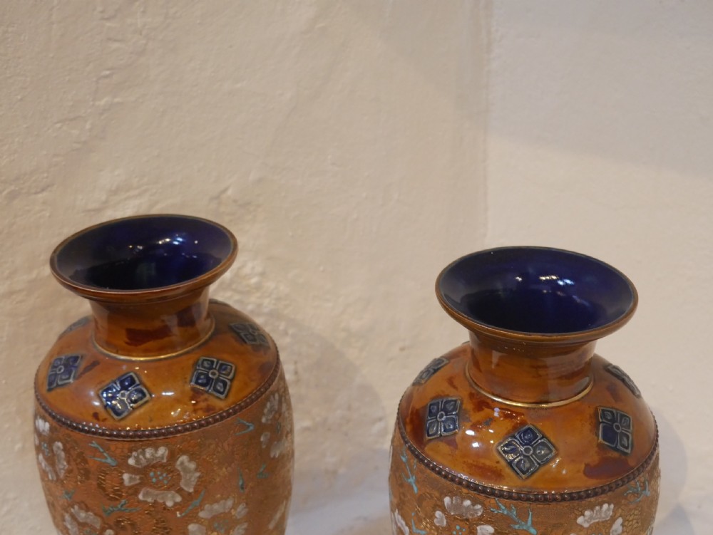 A pair of antique Royal Doulton stoneware vases featuring caramel brown glazing, white floral decorations, and blue foliate accents around the base. View VIII