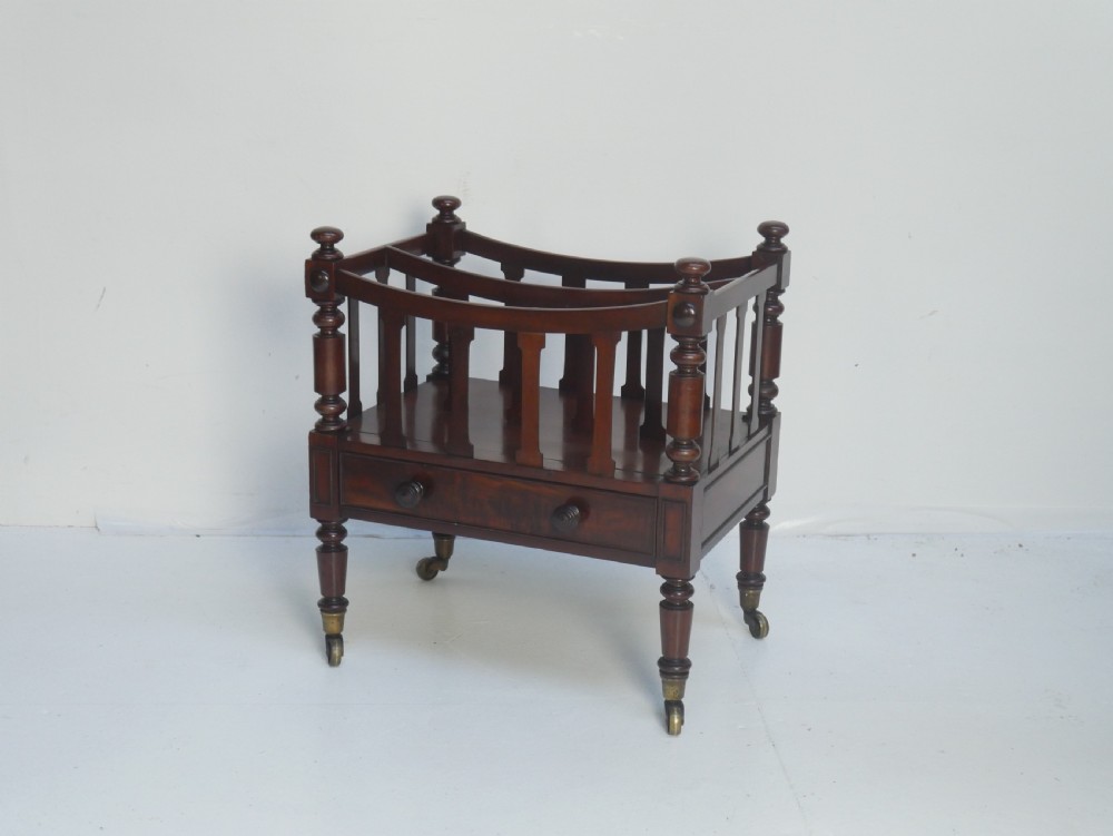 A dark mahogany wooden Canterbury magazine rack featuring slatted dividers, a single drawer with turned knobs, and turned legs with brass castors. View II