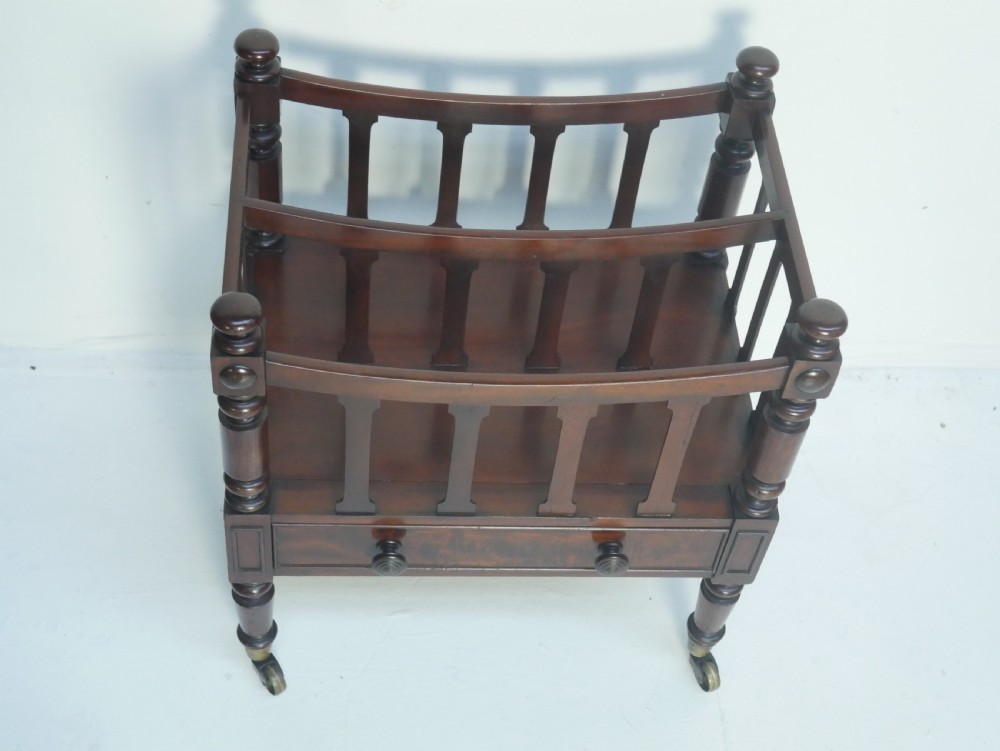 A dark mahogany wooden Canterbury magazine rack featuring slatted dividers, a single drawer with turned knobs, and turned legs with brass castors. View III