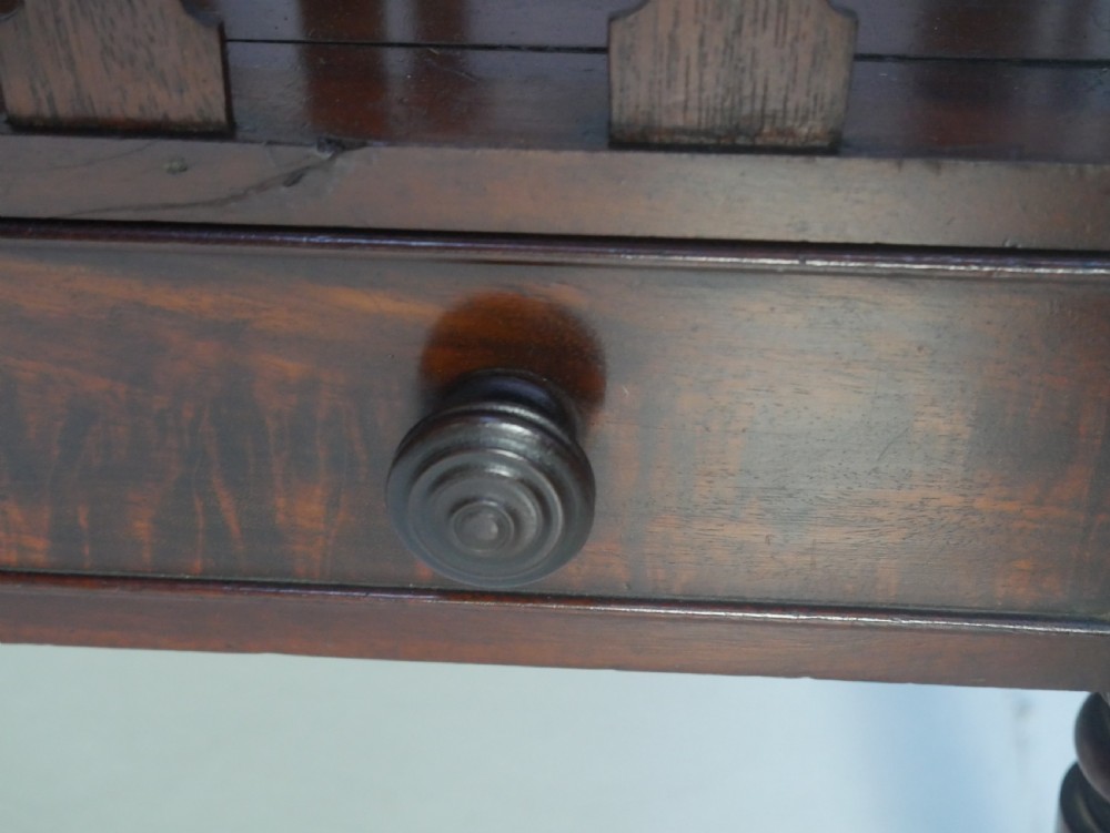 A dark mahogany wooden Canterbury magazine rack featuring slatted dividers, a single drawer with turned knobs, and turned legs with brass castors. View VI