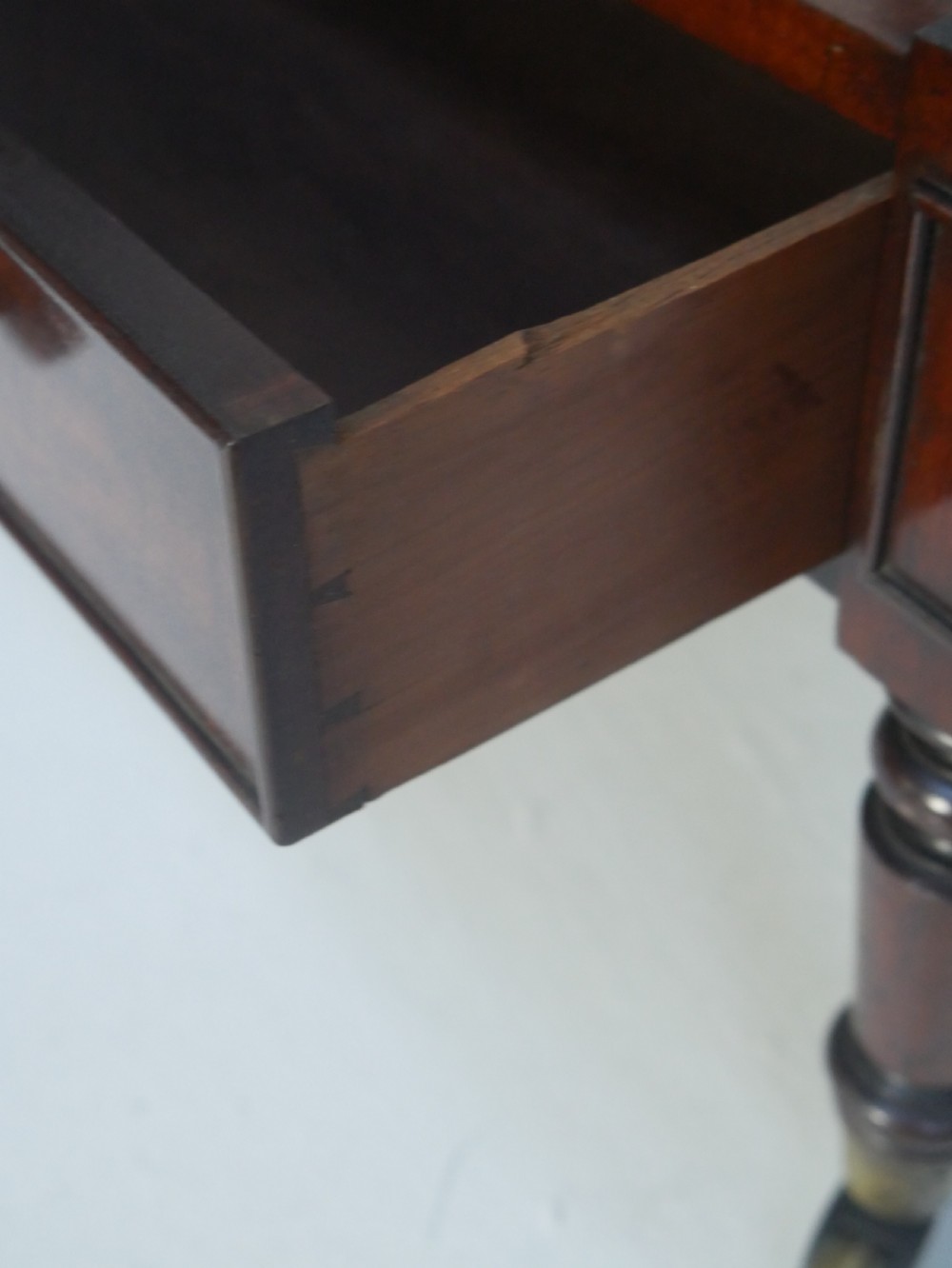 A dark mahogany wooden Canterbury magazine rack featuring slatted dividers, a single drawer with turned knobs, and turned legs with brass castors. View VII