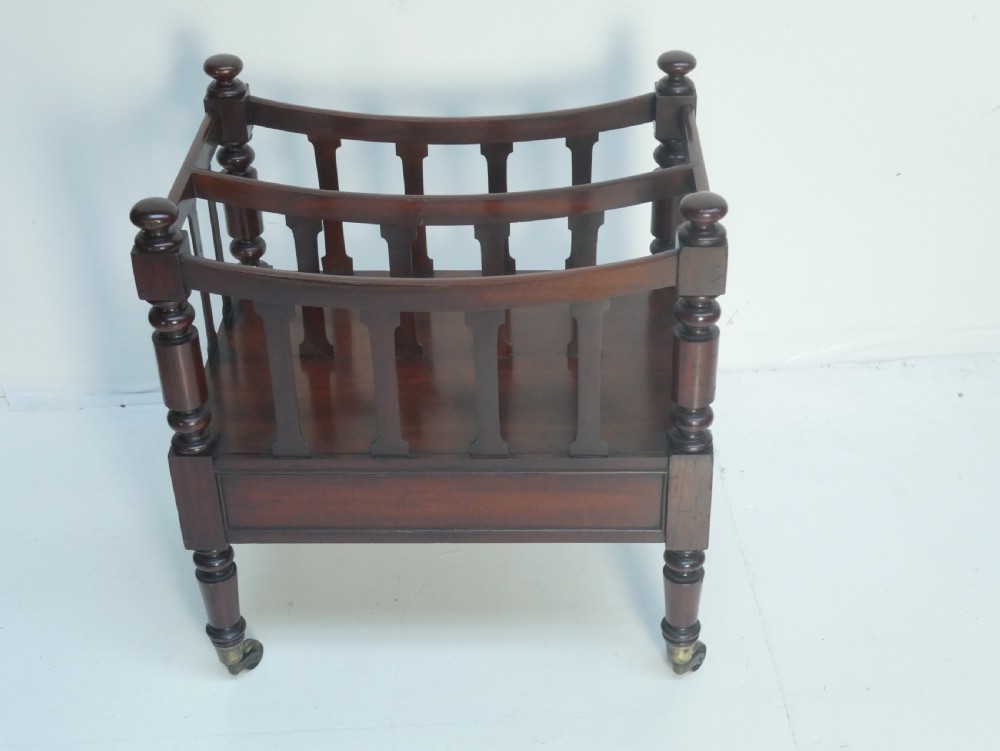 A dark mahogany wooden Canterbury magazine rack featuring slatted dividers, a single drawer with turned knobs, and turned legs with brass castors. View IX