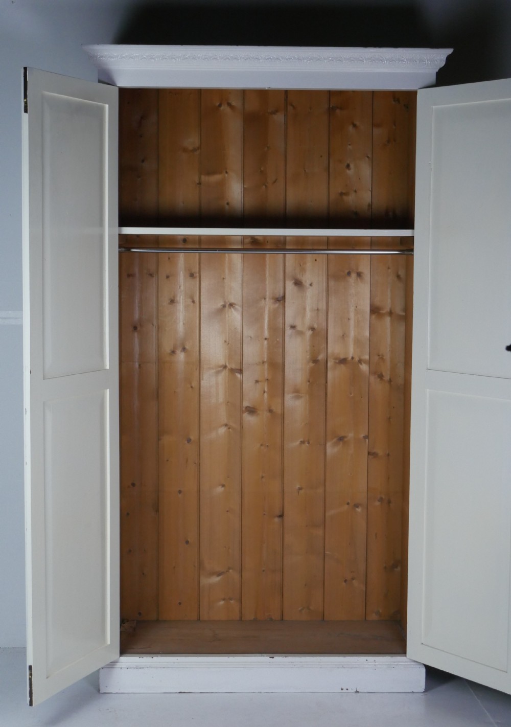A large double-door white painted wooden wardrobe with open doors revealing a natural pine interior featuring a hanging rail and top shelf.