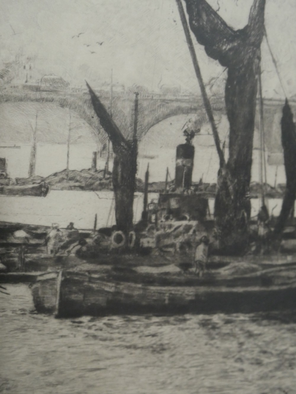 A framed monochrome etching depicting ships and barges on the River Thames with London Bridge in the background. View VIII