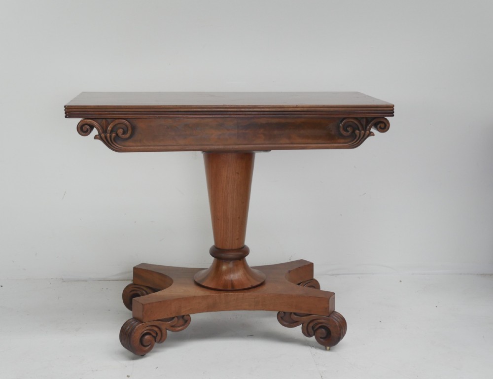 A nineteenth-century mahogany turn-over table with a pedestal stem, carved scroll brackets, and a quadform base on scroll feet.