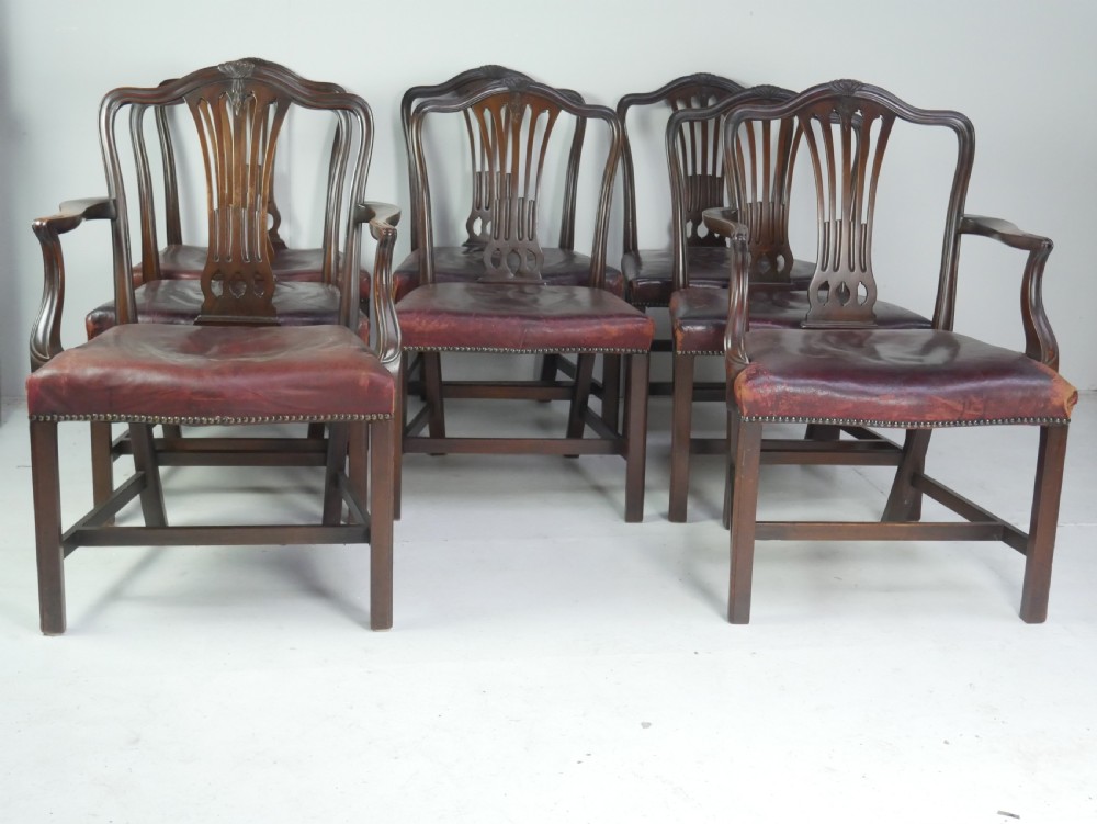 A set of eight mahogany Chippendale style dining chairs featuring pierced splat backs, square legs with stretchers, and burgundy leather seats trimmed with brass studs.