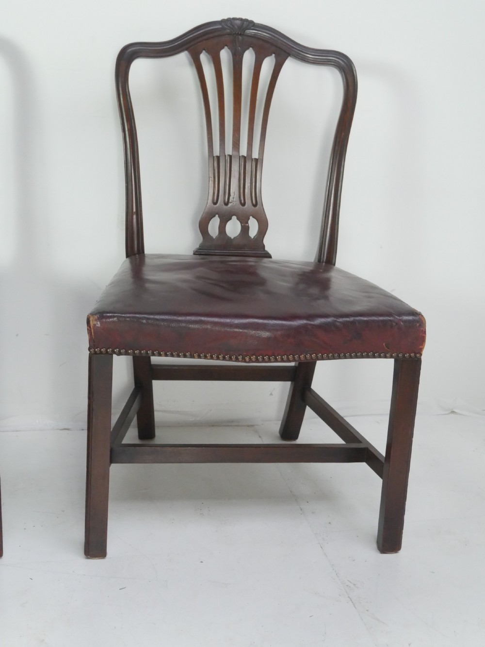A set of eight mahogany Chippendale style dining chairs featuring pierced splat backs, square legs with stretchers, and burgundy leather seats trimmed with brass studs. View II